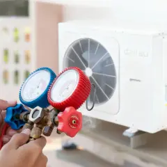 Manos sostienen manómetros para detectar fuga aire acondicionado casa. El equipo de refrigeración está montado en la pared.